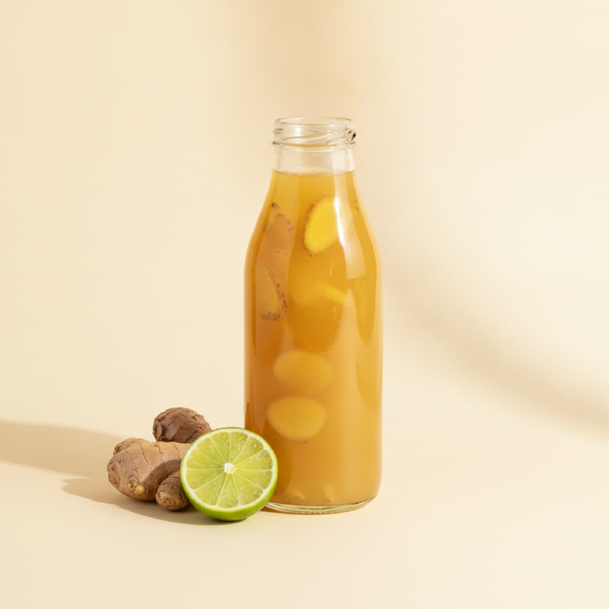 Glass bottle of golden ginger juice with fresh ginger root and lime
