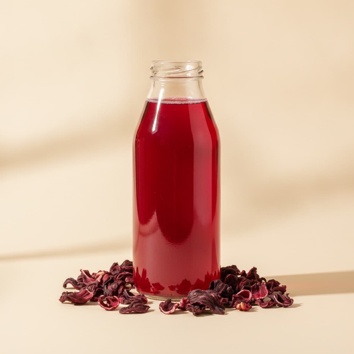 Glass bottle of deep red hibiscus juice with dried hibiscus flowers